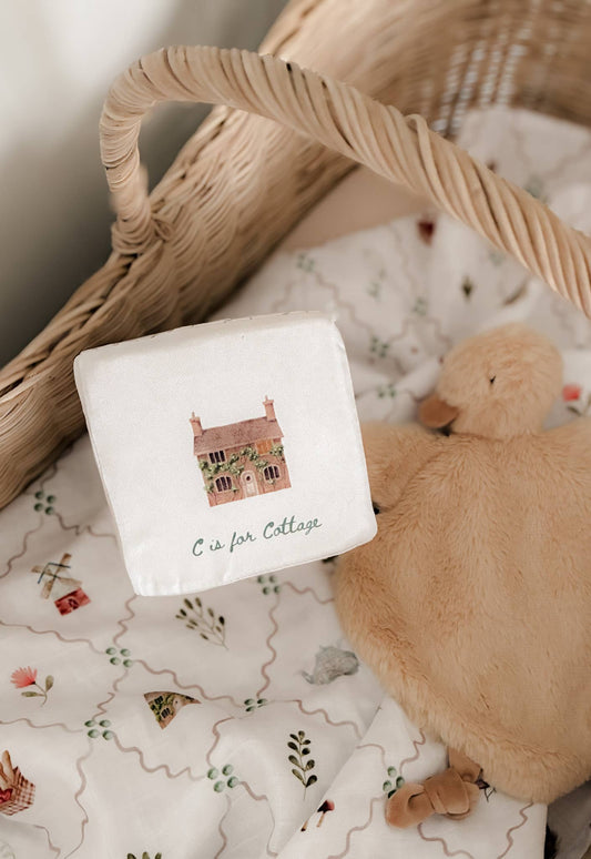 White square with letter 'C' for Cottage design, teddy bear, and wicker basket on patterned fabric.