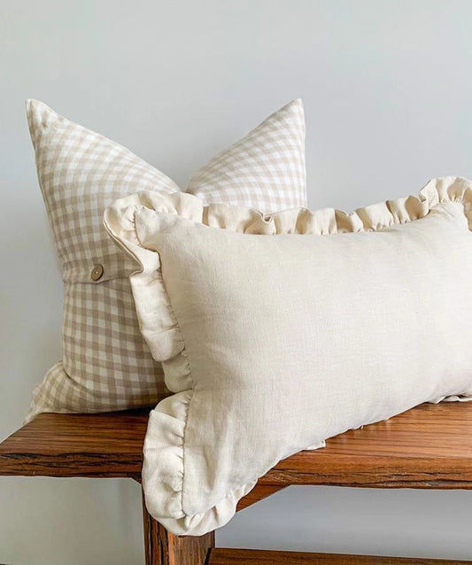 Two decorative pillows on a wooden bench against a light gray wall.