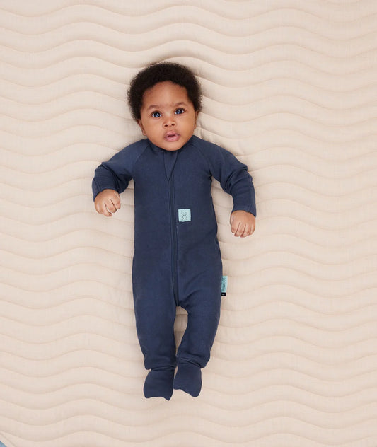 Baby wearing a blue onesie lying on a beige textured surface