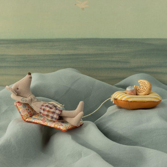Stuffed animal lying on a floral mat with a small boat, all on a textured green surface.