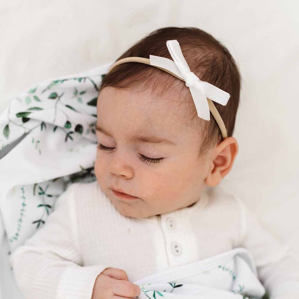 Baby wearing a white headband with a bow, wrapped in a green and white blanket.