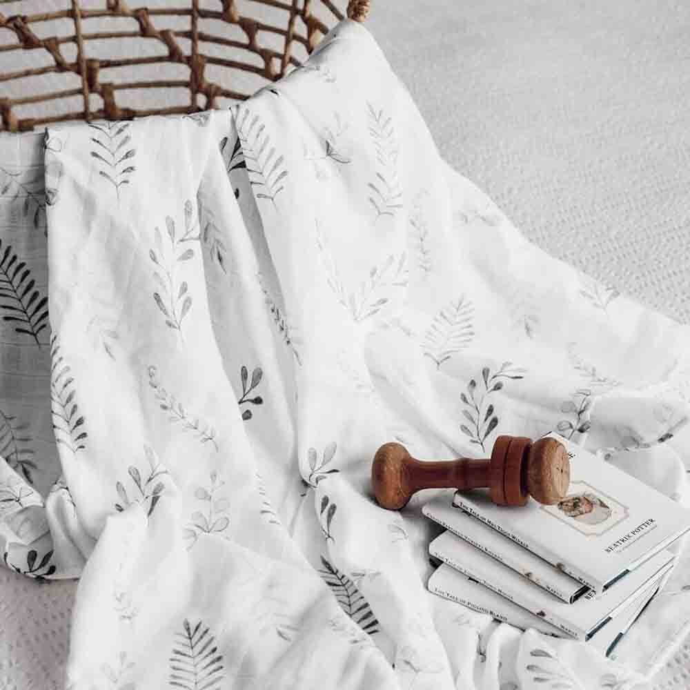 White patterned blanket draped over a bed with a wooden block and books underneath.