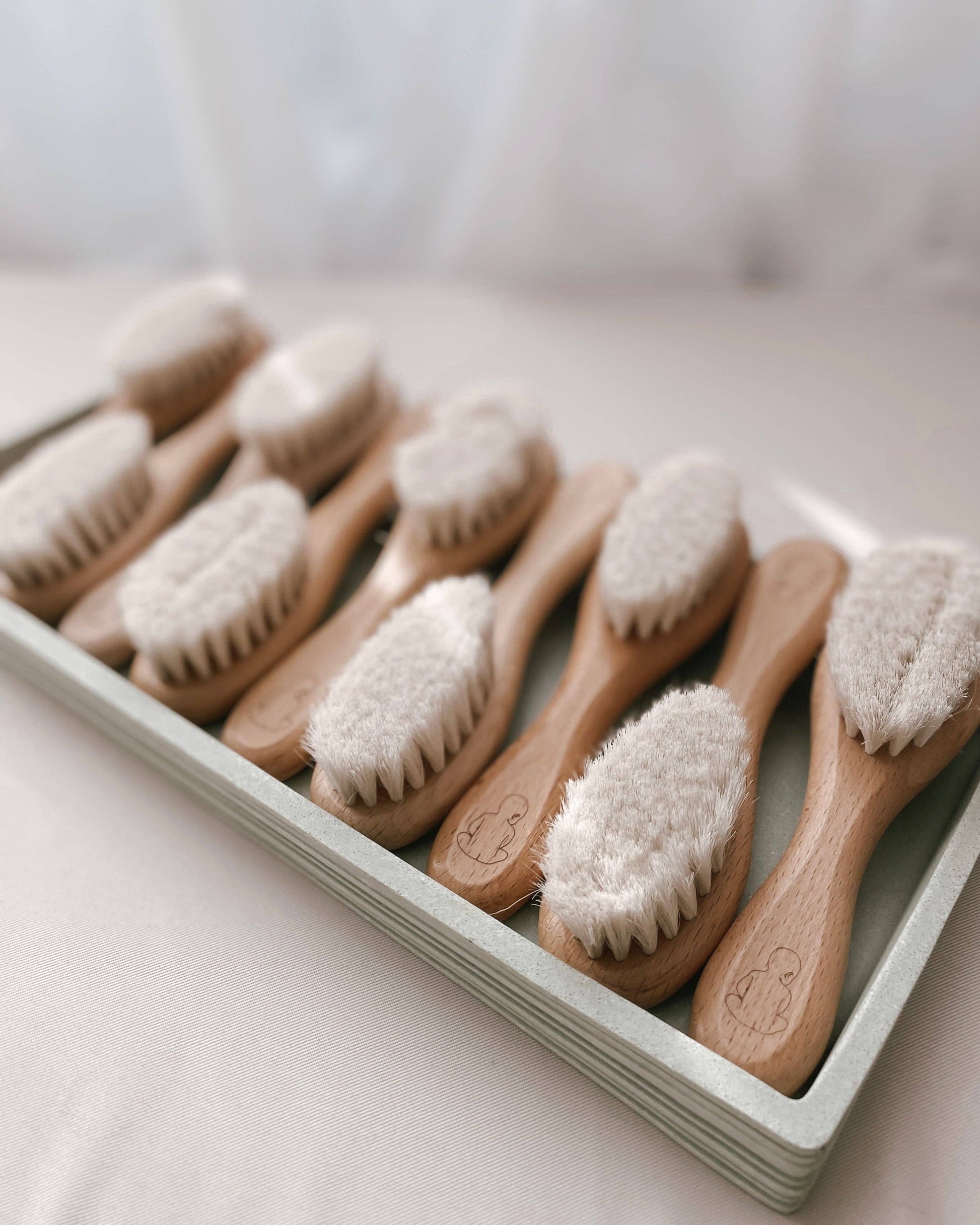 Set of wooden baby brushes with soft bristles in a white tray on a light surface.