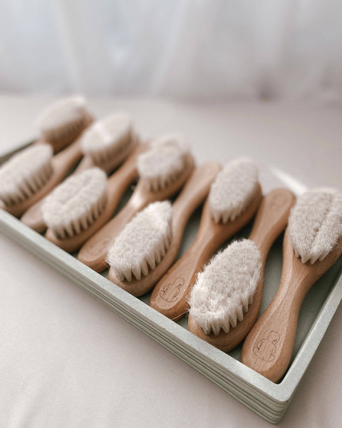 Set of wooden baby brushes with soft bristles in a white tray on a light surface.
