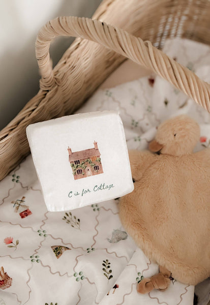 White square with letter 'C' for Cottage design, teddy bear, and wicker basket on patterned fabric.