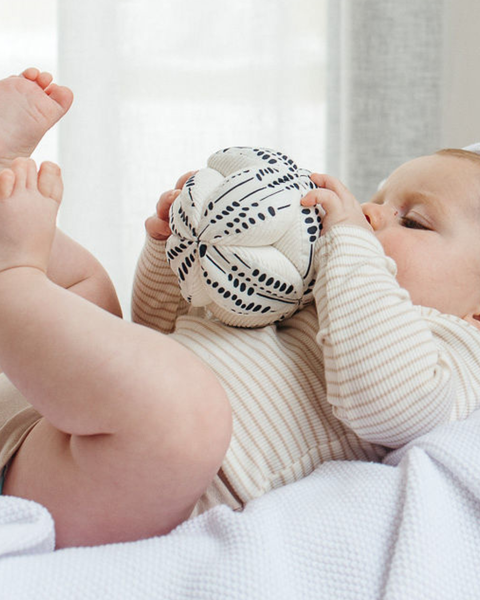 Baby playing with a textured ball on a white blanket