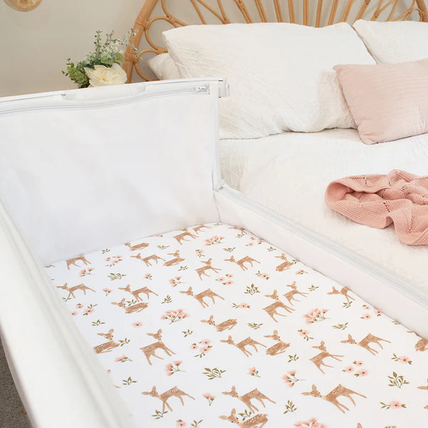 Baby crib with floral and deer patterned sheet in a bedroom setting.