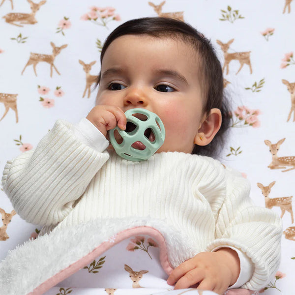 Baby holding a green teething ring with a floral and deer patterned background