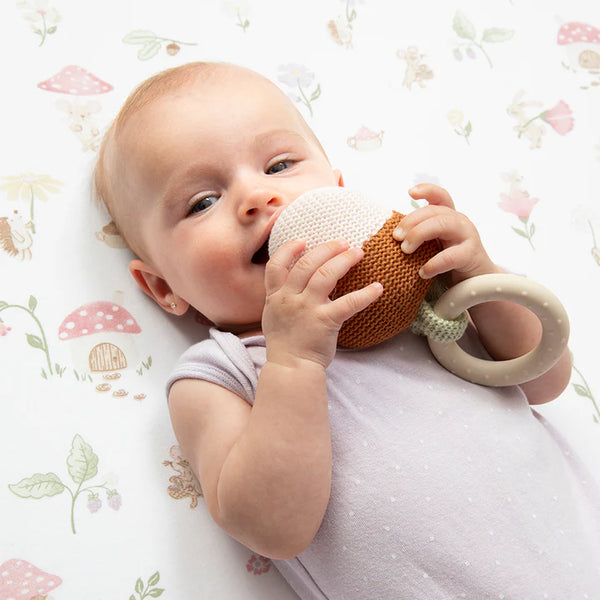 Baby lying on a floral-patterned blanket with a teething ring.