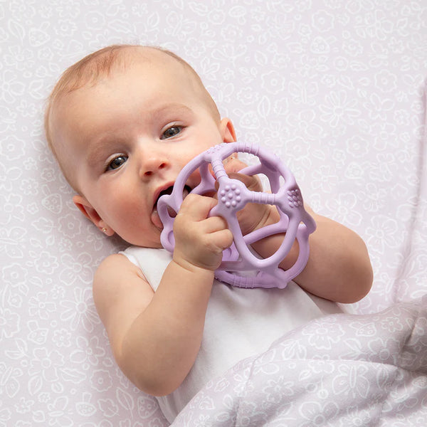 Baby holding a purple teething ring on a white textured background