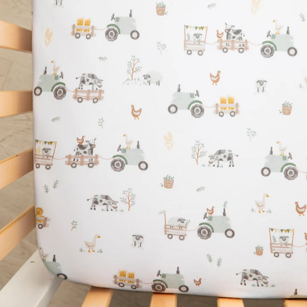 Crib sheet with farm-themed pattern featuring tractors, trucks, and animals on a white background.