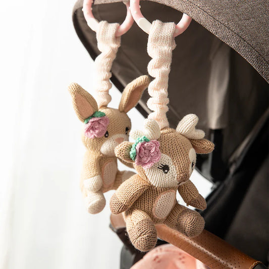 Knitted deer toys hanging from a stroller handle with a blurred background