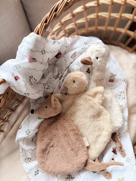 Two plush toys, a deer and a duck, in a wicker basket with a patterned cloth.