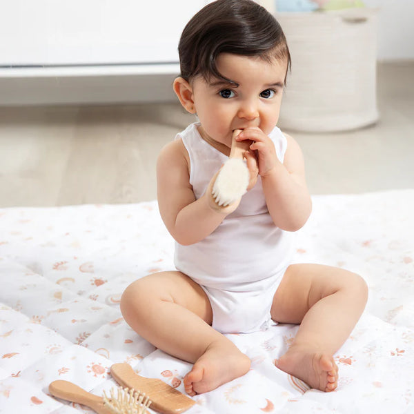 Baby sitting on a bed holding a wooden brush