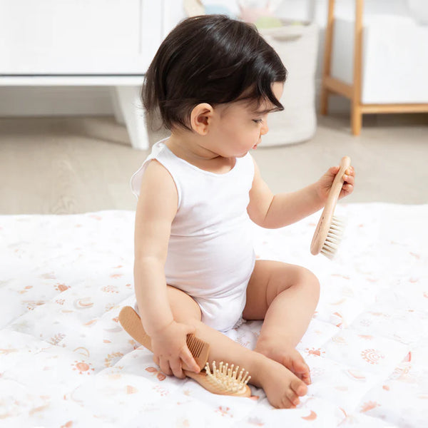 Baby sitting on a bed holding wooden brushes
