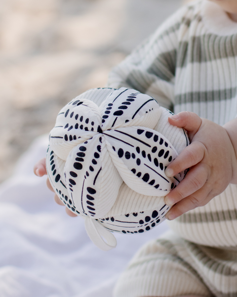 Hand holding a knitted ball with black patterns against a blurred background
