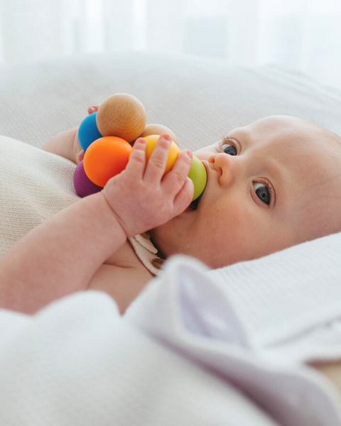 Baby holding a colorful teething ring with a blurred white background