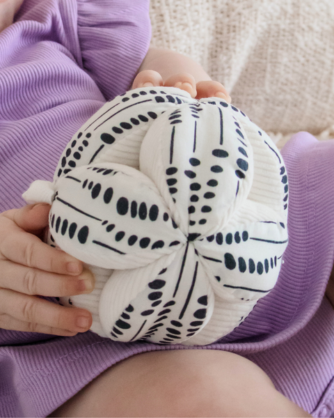 White knot pillow with black patterns held by a person wearing a purple garment.