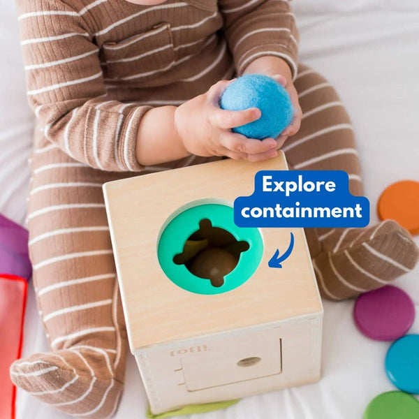 Child playing with a wooden shape sorter toy, holding a blue ball.
