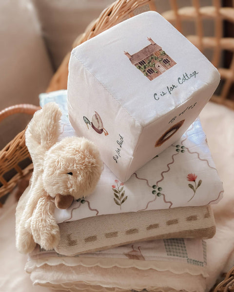 Stack of baby blankets with a soft toy and a decorative block on a textured surface.