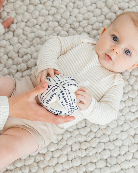 Baby holding a black and white patterned ball on a soft, textured surface