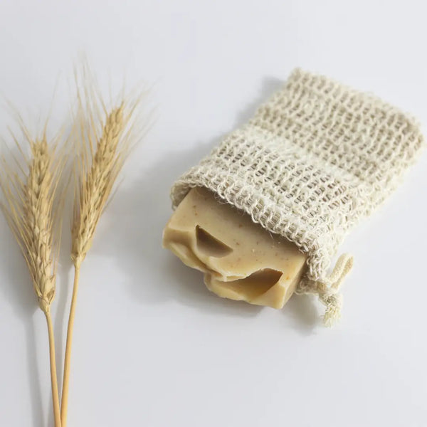 Bar of soap in a natural fiber bag with a stalk of wheat on a light background