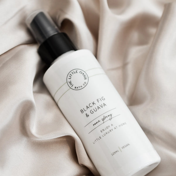 White bottle of 'Black Fig & Guava' body spray on beige fabric