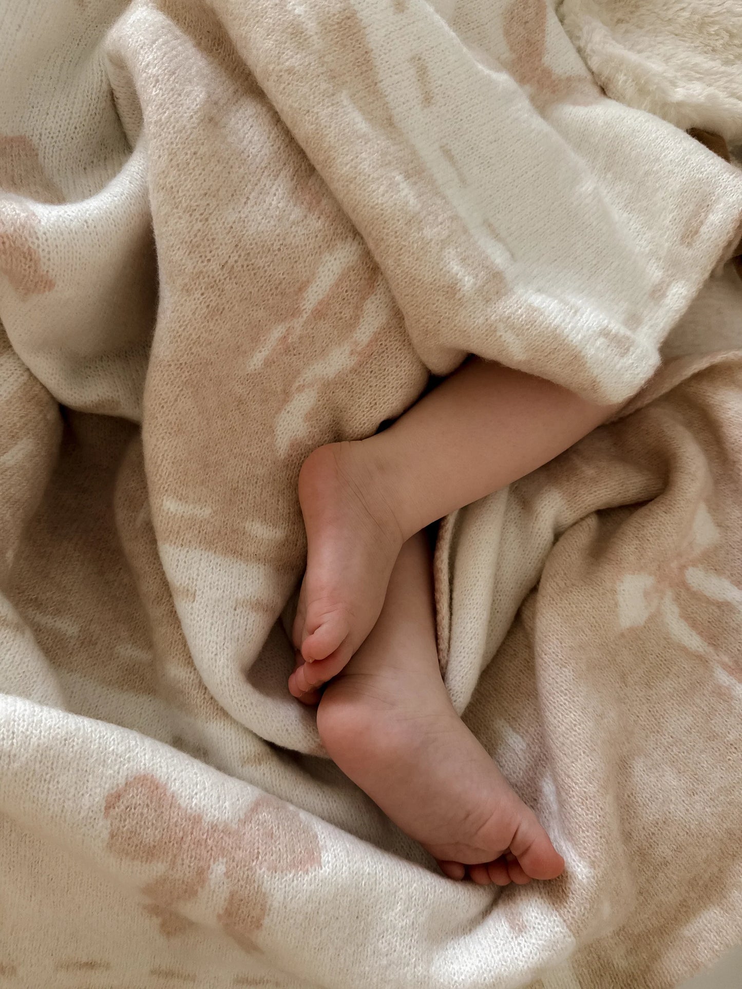 Close-up of a baby's feet peeking out from under a soft beige blanket.