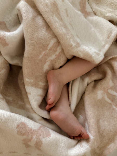 Close-up of a baby's feet peeking out from under a soft beige blanket.