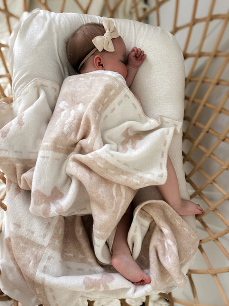 Baby wrapped in a blanket with a bow, lying on a textured surface