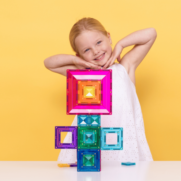 Child holding colorful magnetic building blocks against a yellow background