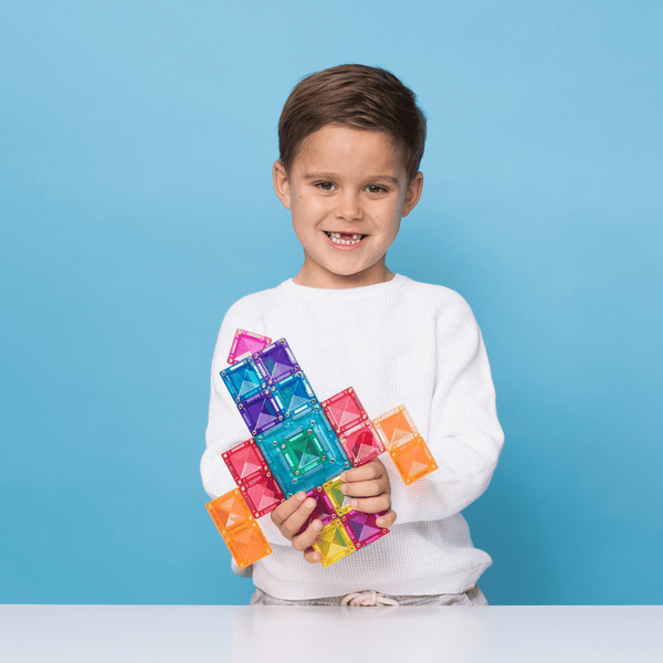 Child holding colorful magnetic building blocks against a blue background
