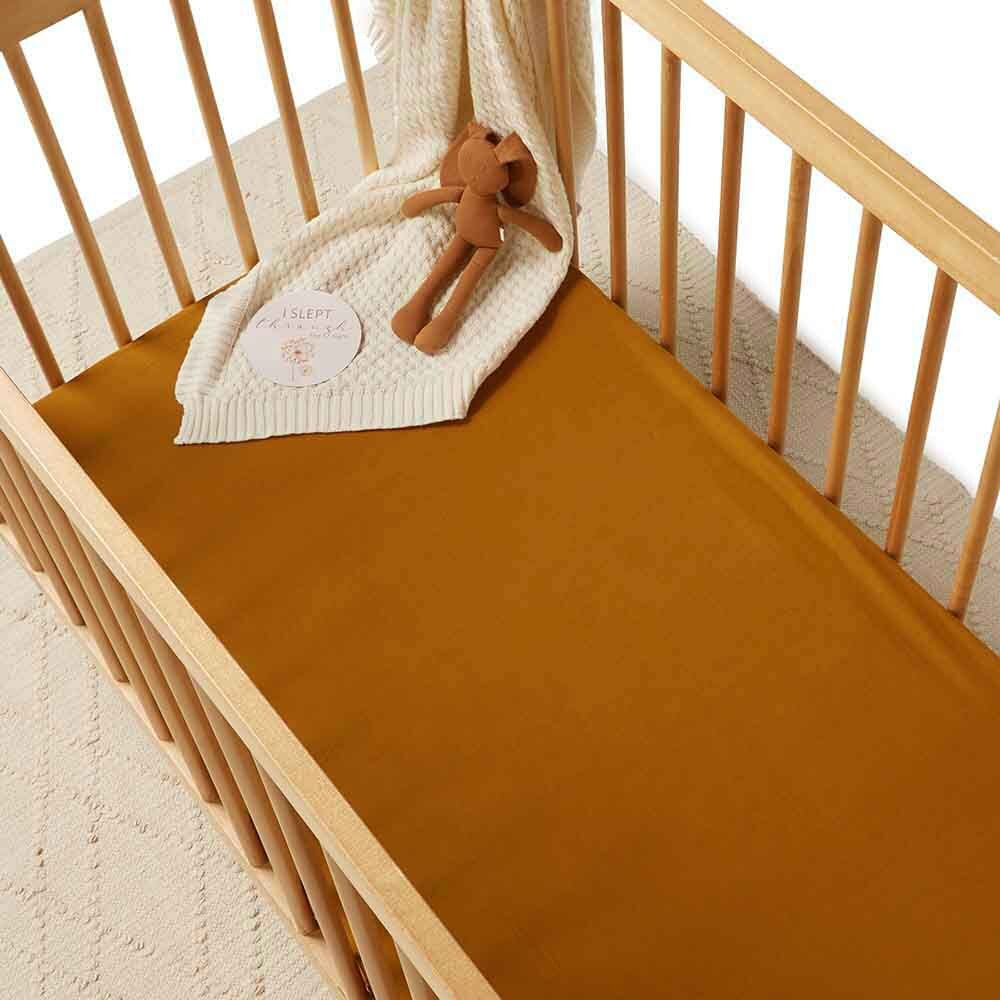 Crib with bronze fitted sheet, white blanket, and wooden toy on a light background