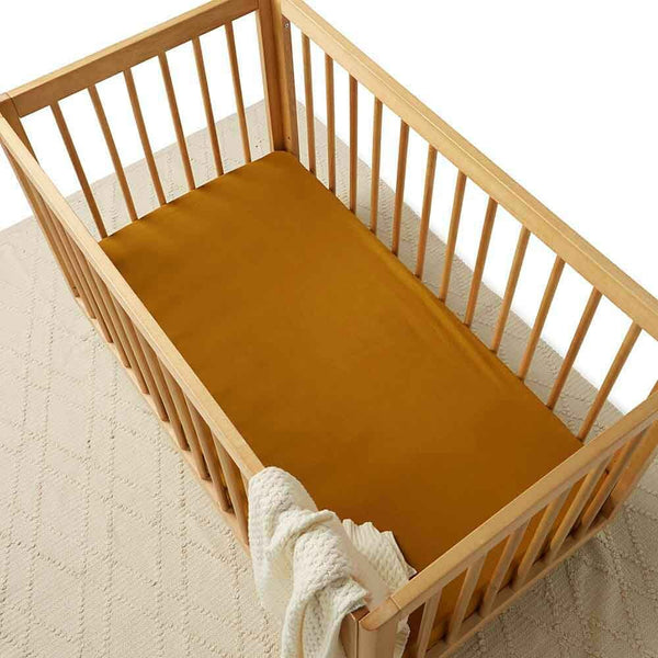Wooden crib with mustard yellow mattress cover and white blanket on a neutral background