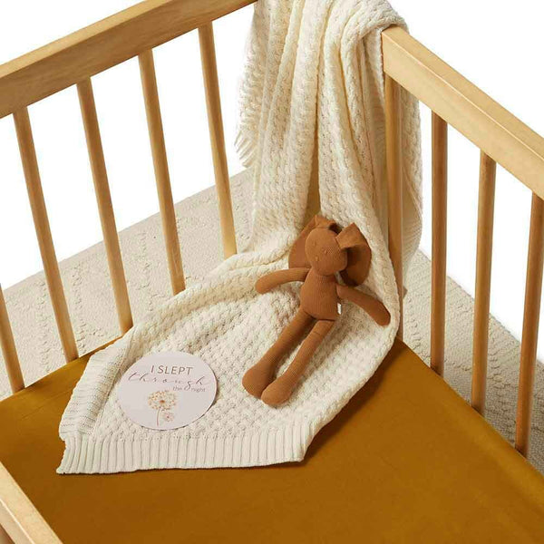 Crib with a white textured blanket, brown teddy bear, and a sign on a white background