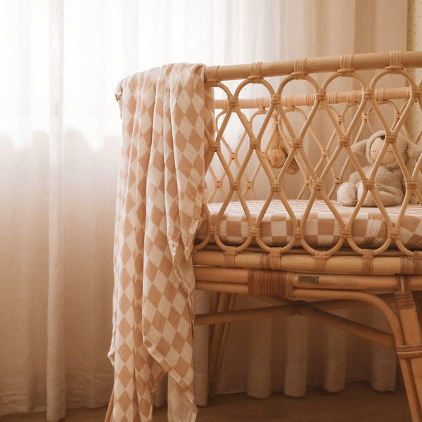 Wicker crib with checkered blanket and teddy bear in a softly lit room