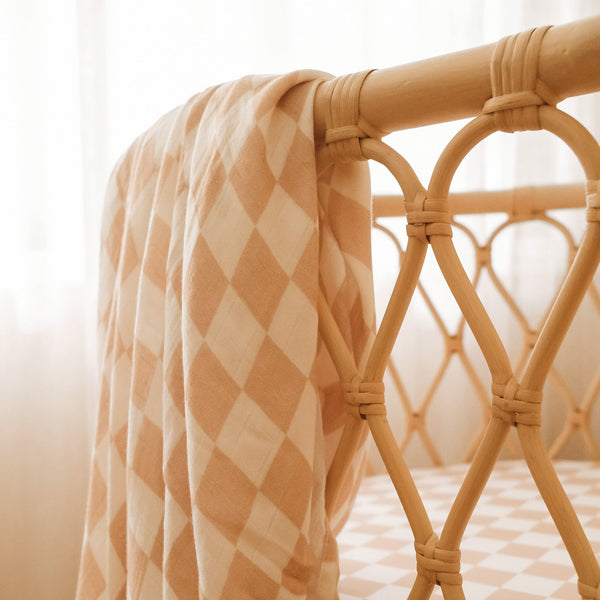 Checkered blanket draped over a wicker bassinet with a blurred background