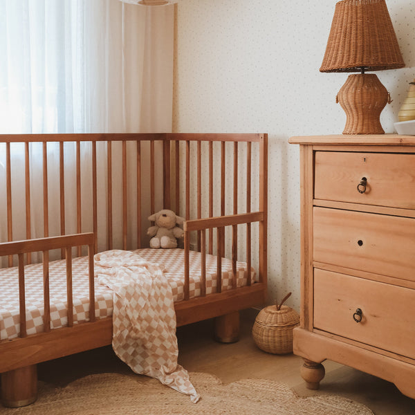 Nursery room with wooden crib and dresser, featuring a teddy bear and lamp.