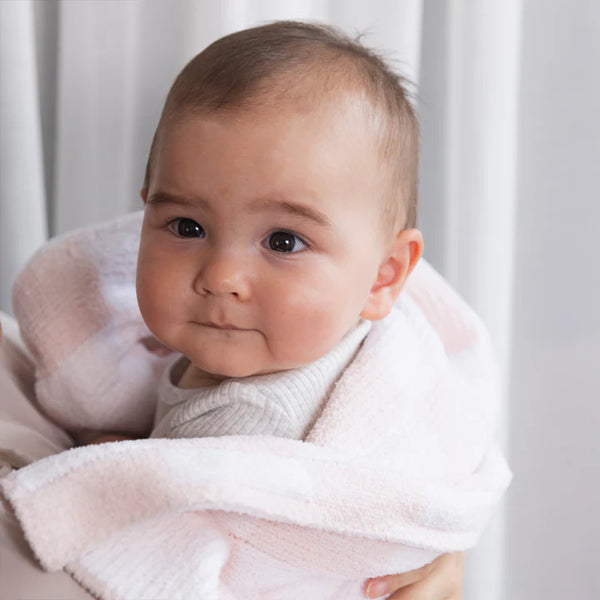Baby wrapped in a pink blanket with a neutral background