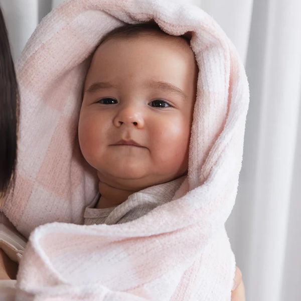 Baby wrapped in a pink towel, looking at the camera with a neutral expression.