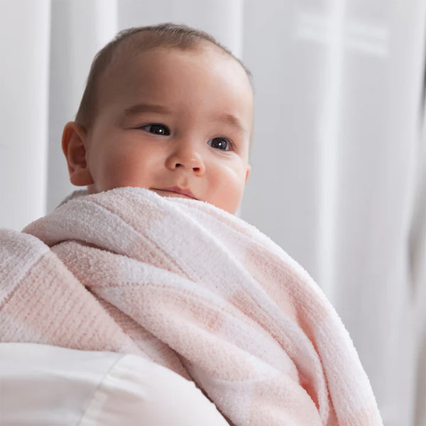 Baby wrapped in a pink blanket with a white curtain background