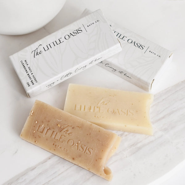Two bars of soap from 'The Little Oasis' on a white surface with packaging.