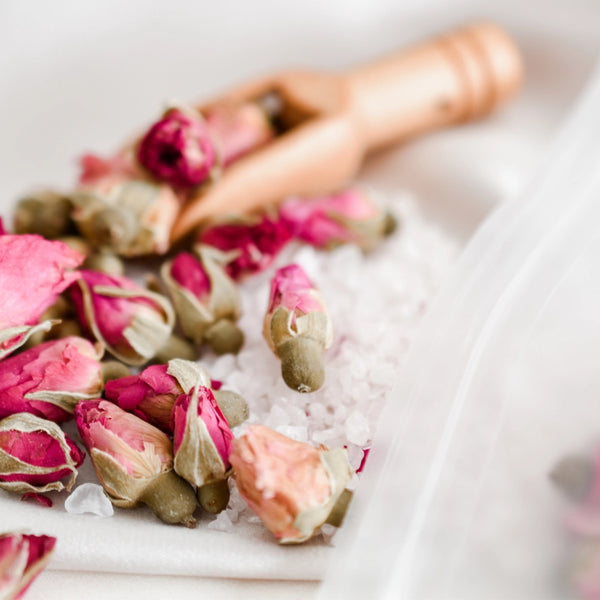 Dried pink rose petals on a white surface with a blurred hand in the background