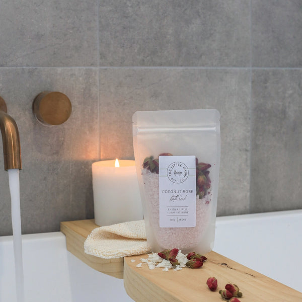 Bath salts packaging with a candle and towel on a bathtub ledge.