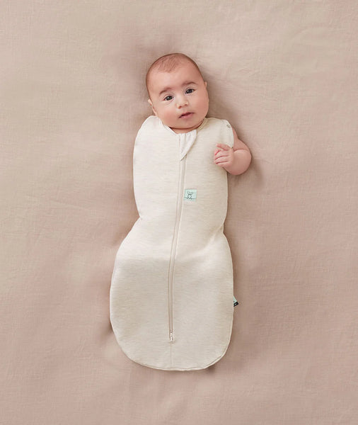 Baby wrapped in a white swaddle on a beige blanket