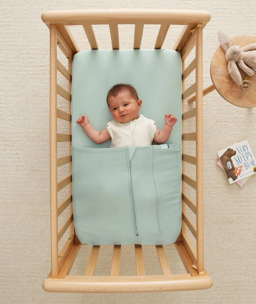 Baby lying in a light blue crib sheet inside a wooden crib.