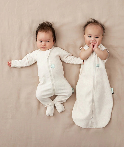 Two babies wearing white sleep sacks on a beige blanket