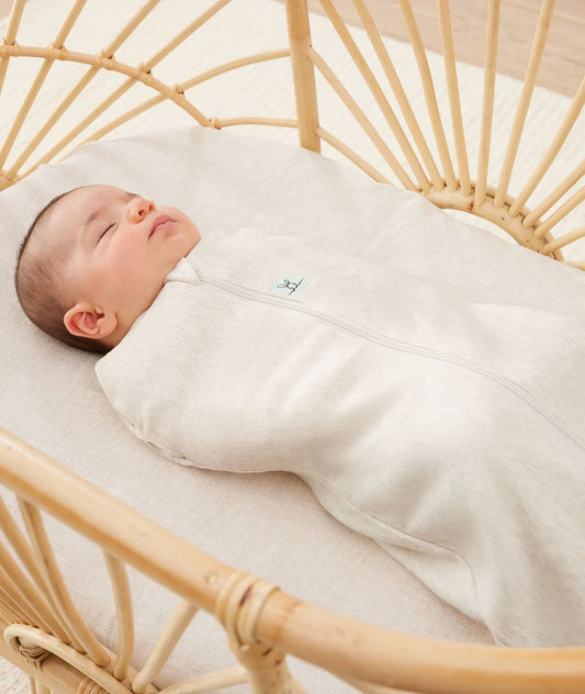 Newborn baby swaddled in a white blanket lying in a rattan crib.