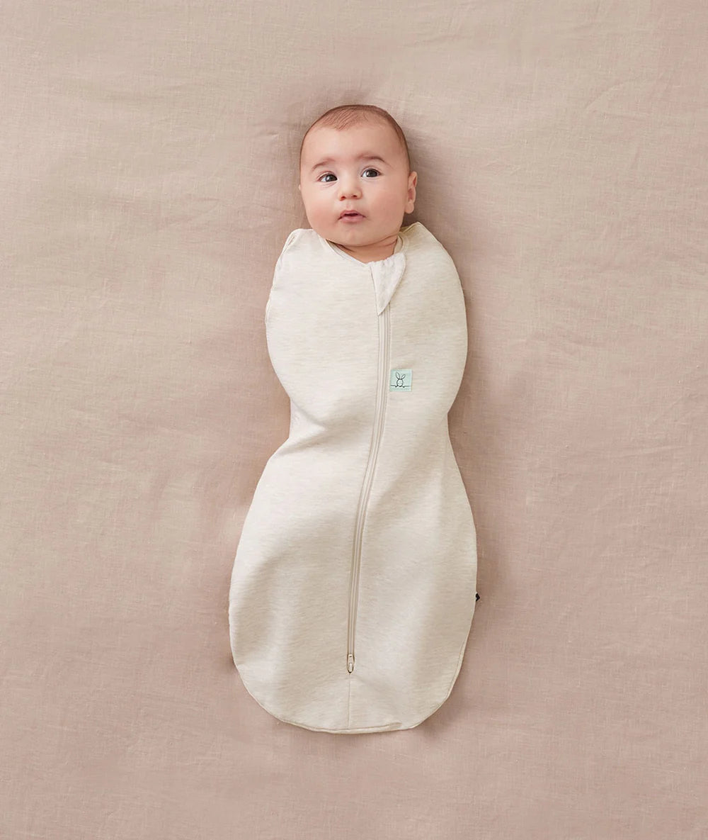 Baby wrapped in a white swaddle on a beige blanket