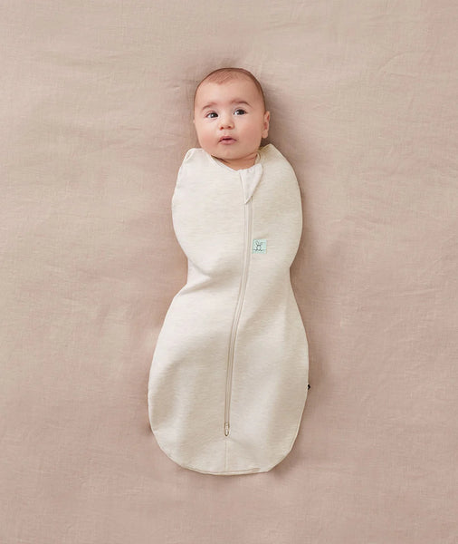 Baby wrapped in a white swaddle on a beige blanket